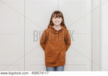 Portrait Of A Tein-haired Girl 9 Years Old At Home In A Brown Sweater, Looking At The Camera And Smi