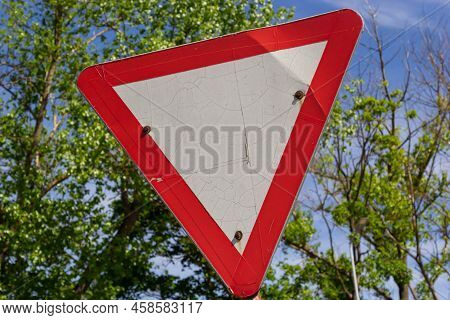 Close-up Of Give Way Road Sign. Red And White Triangle. Green Trees And Blue Sky On Background