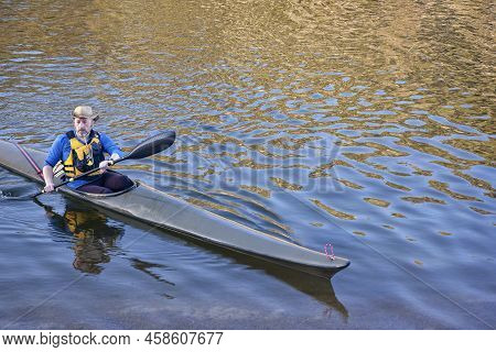 Mature Male Paddler In A Long And Narrow Racing Sea Kayak With A Wing Paddle On A Lake With Gold Ref