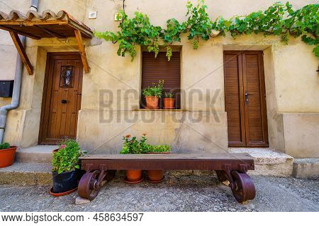 Nice Facade Of Stone Houses With A Vine With Grapes Climbing The Wall And Wooden Bench At The Door.