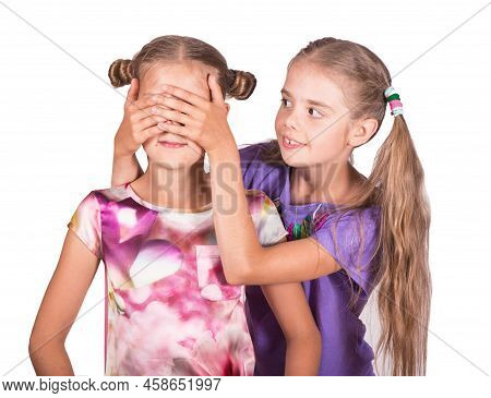 Children Play And Joke. One Girl Closes The Eyes Of Another. Photo Isolated On White Background