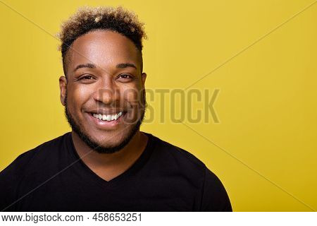 A Young Stylish Black Man In An Everyday Black T-shirt Smiles Against A Yellow Background At A Close