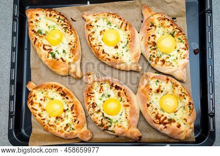Adjarian Khachapuri In The Shape Of A Boat. Six Portions On A Baking Tray As Seen From Above. A Fluf