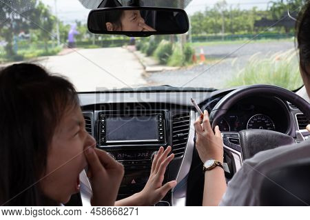 Asian Woman Smoking Cigarette While Driving Inside The Car And The Child Choking Of Smoke, Bad Smell