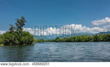 The Bed Of The Calm Blue River Bends Between The Green Banks. Mountains On The Background Of Azure S