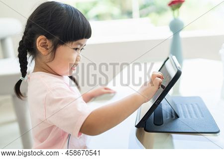 Asian Girl Looking And Touch On Tablet Screen Attentively. Overstimulated Children Concept. Too Much