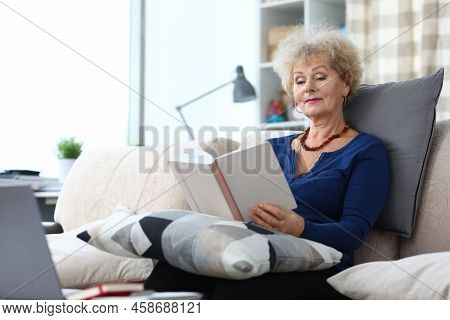 Elderly Woman Is Reading Book At Home On Couch. Home Leisure Pensioners Concept