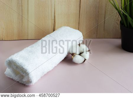 Rolled White Towel With Cotton Flower On The Pink Table With Wooden Background