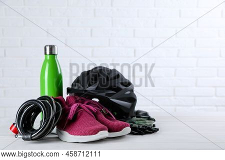 Different Cycling Accessories On White Wooden Table Against Brick Wall, Space For Text