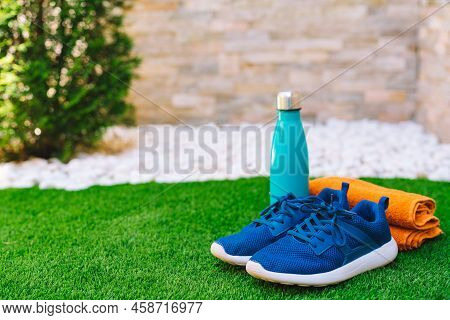 Close-up Of Objects And Accessories To Practise Sports On Green Grass Field. Weights, Towel, Bottle 