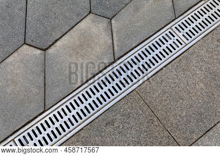 The Grid Of The Rainwater Drainage System On The Sidewalk Made Of Stone Paving Slabs. Top View