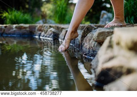 Unrecognizable Young Woman Is Dipping Her Foot In Cool Water Of Pond, Refreshing And Hardening Conce