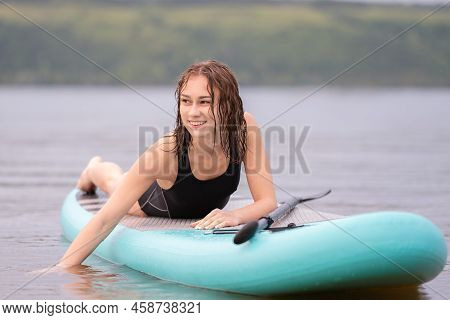 A Beautiful Girl Is Floating On A Supboard On A River. Young Woman Supsurfing At Sunrise.