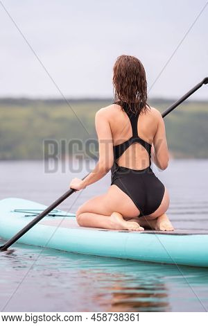 A Beautiful Girl Is Floating On A Supboard On A River. Young Woman Supsurfing At Sunrise.