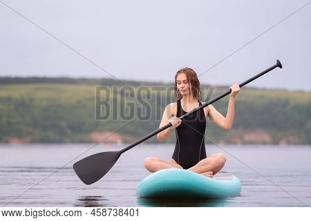 A Beautiful Girl Is Floating On A Supboard On A River. Young Woman Supsurfing At Sunrise.