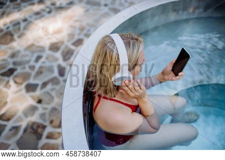 Rlaxed Woman Wearing Headphones Listening To Music And Sittin In Hot Tub, Summer Vacation Concept.