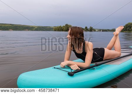 A Beautiful Girl Is Floating On A Supboard On A River. Young Woman Supsurfing At Sunrise.