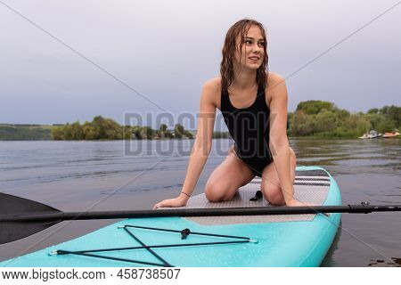 A Beautiful Girl Is Floating On A Supboard On A River. Young Woman Supsurfing At Sunrise.