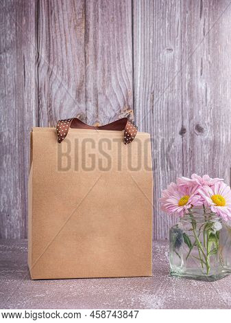 Brown Paper Bag Packaging With Ribbon Handles Placed On A Gray Stone Background With A Wooden Wall. 