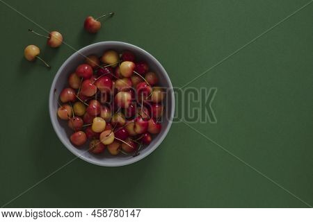 Top View On Light Gray Plate With Yellow Cherries On Green Background With Copyspace
