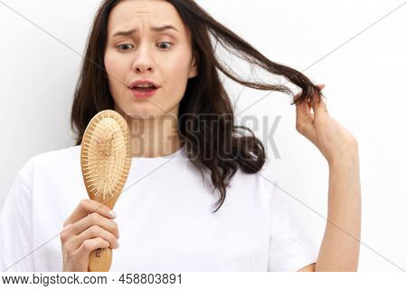 A Sad, Upset, Puzzled Woman With Long Black Hair Stands In A White T-shirt On A Light Background And
