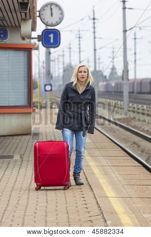 una giovane donna con la valigia in attesa sulla piattaforma di una stazione ferroviaria sulla loro treno. ritardo treno