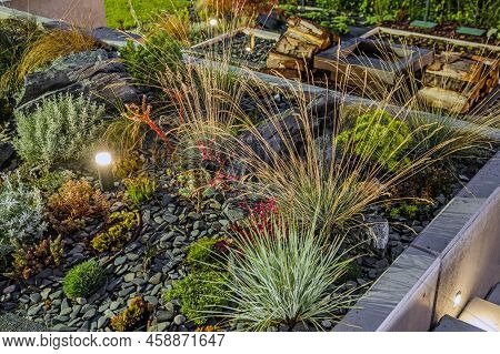 Beautiful Rockery Garden Illuminated At Night By Led Outdoor Lighting. Outdoor Backyard Fireplace In