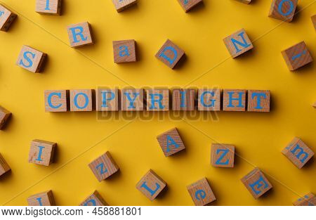 Plagiarism Concept. Word Copyright Made Of Wooden Cubes On Yellow Background, Top View