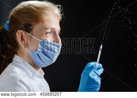 The Doctor Sprays From A Syringe Against A Black Background. The Doctor Smiles Under His Protective 