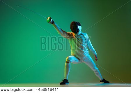 Studio Shot Of Young Man, Fencer With Smallsword Practicing Fencing Isolated On Green Background In 