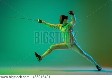 Studio Shot Of Young Man, Fencer With Smallsword Practicing Fencing Isolated On Green Background In 