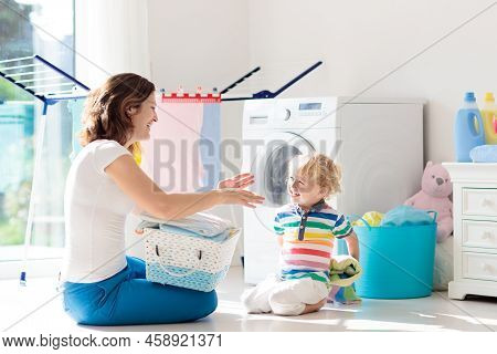 Mother And Kids In Laundry Room With Washing Machine Or Tumble Dryer. Family Chores. Modern Househol