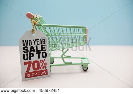 Mid Year Sale Up To 70% Text Message On Price Tax With Shoppint Trolley Cart On Blue Andp Pink Backg