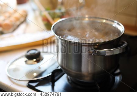 Shiny Pot With Boiling Water On Stove Indoors. Space For Text