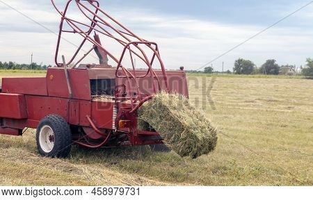 Farm Hay Field. The Process Of Harvesting Hay For Cattle, The Tractor Makes Bales In The Field.