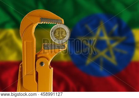 Ethiopian One Birr Coin Held In An Orange Plumber Wrench On The Background Of The Ethiopian Flag. Re
