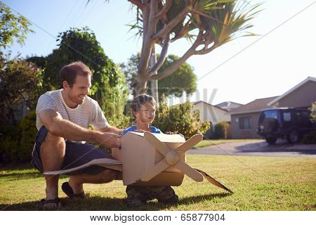 son and dad playing with toy aeroplane in the garden at home having fun together and smiling