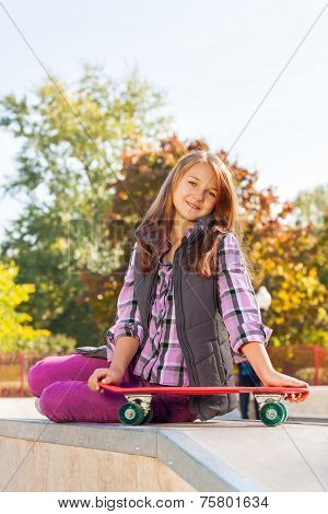 Positive girl holds skateboard sits on ground