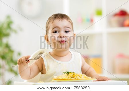 cute kid boy in a highchair for feeding with a fork and a pasta