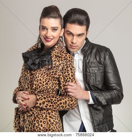 Attractive fashion man holding his girlfriend while she is hlding her fingers crossed, both looking at the camera.