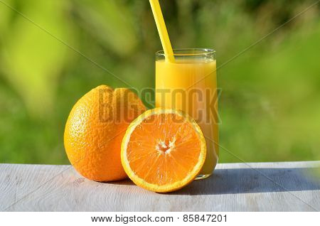 glass of delicious orange juice and oranges on table in garden
