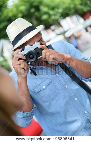 Trendy guy with hat taking picture of woman with vintage camera