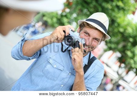 Trendy guy with hat taking picture of woman with vintage camera