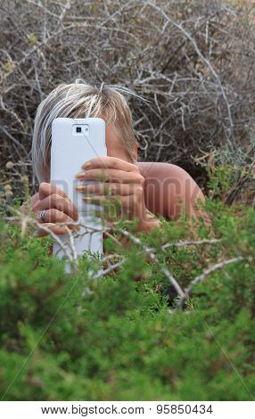 A Girl With Smart Phone Hiding In The Bushes Outdoors