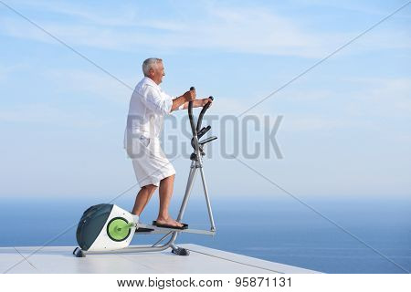 healthy senior man working out on gym treadmill machine at modern home terace with ocean view