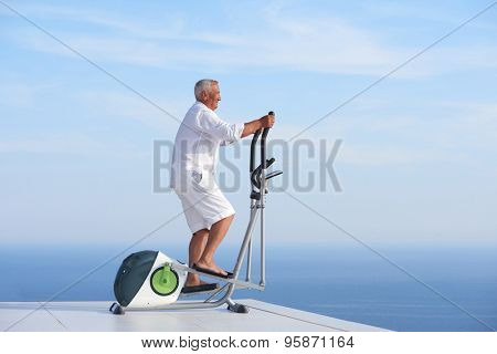healthy senior man working out on gym treadmill machine at modern home terace with ocean view