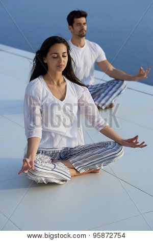 young couple practicing yoga at sunset in modern home terace with ocean and sunset in background