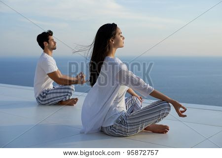 young couple practicing yoga at sunset in modern home terace with ocean and sunset in background