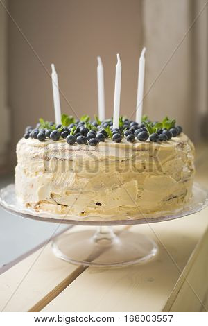 Closeup of white homemade birthday cake with blueberries and candles on wooden table. Celebration party cake.