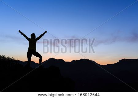 Woman hiking silhouette in mountains sunset and ocean. Female hiker climber or trail runner with arms outstretched on mountain top looking at beautiful night sunset inspirational landscape.